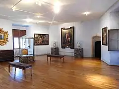 Photographie en couleur d'une salle d'exposition avec des tableaux et des objets d'art.