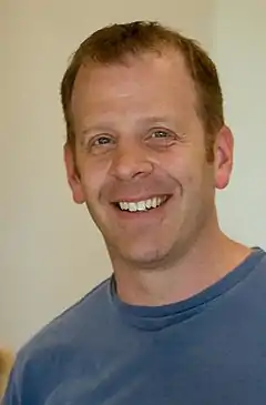 Photo d'un homme vu de face en train de sourire cadré en gros plan.