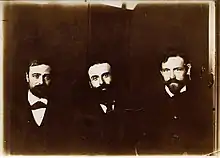 Photographie en noir et blanc de trois hommes prenant la pose.