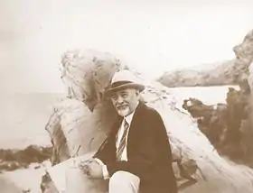 Photographie d'un personnage assis sur des rochers en bord de mer.