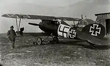 Photo en noir et blanc d'un homme adossé à l'aile d'un avion biplan.