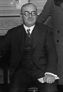 Portrait de Claudel en 1925 : assis et appuyant une main tenant un livre sur son genou gauche