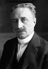 Portrait photographique en noir et blanc d'un homme à la moustache et aux cheveux grisonnants, brossés en arrière ; il porte une cravate, une chemise à faux col et un costume trois pièces