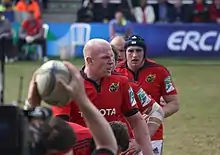 Alignement de joueurs pour une touche. Au premier rang, le ballon, tenu au-dessus de sa tête par le talonneur.