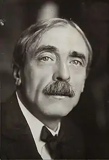 Photographie noir et blanc d'un homme moustachu, de face.