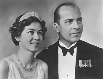 Photographie d'un couple, dont la femme porte une robe de soirée claire, un diadème et un collier de diamants et l'homme une tenue militaire.