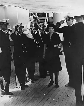 Photographie en noir et blanc montrant un groupe de militaires en compagnie d'une femme sur le pont d'un bateau.