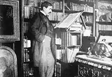 Paul Bourget dans son bureau, rue Barbet – de – Jouy, debout devant un pupitre.