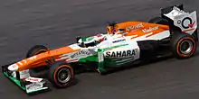 Photographie d'une monoplace de Formule blanche, orange et verte, vue de profil, de haut.