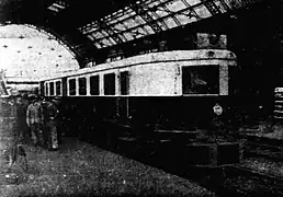 Photographie en noir et blanc d'un autorail à quai dans une gare avec verrière.