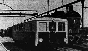 Photographie en noir et blanc montrant une vue de trois quart avant de la Pauline type 1 à côté d'une locomotive à vapeur.