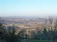 Au premier plan, le stade communal dans l’ombre ; puis les champs en contrebas ; puis des collines avec une agglomération (Reillanne) ; tout au fond, la masse sombre de la montagne de Lure.