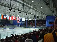 Photographie d'une patinoire vue depuis les gradins, des drapeaux suspendus au-dessus de la patinoire.