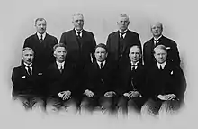 Photo de groupe en noir et blanc de neuf hommes, quatre debout et cinq assis