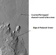 Quadrangle d'Oxia Palus : cratère à piédestal et crête (HiRISE). La crête est un ancien lit de rivière, inversé par l'érosion. le cratère a percé la crête, il est donc plus récent.