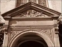 Détail d'une porte en pierre. Le dessus est triangulaire, avec les têtes de deux chérubins dessous. Sur l'arche immédiatement au-dessus de l'entrée, les mots « ascendat oratio descendat Gratia »; une rose et un chardon sur les panneaux adjacents