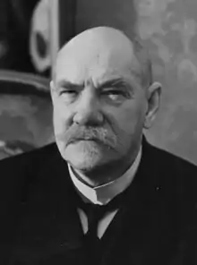 Photo en buste en noir et blanc d'un homme âgé chauve et portant une moustache blanche