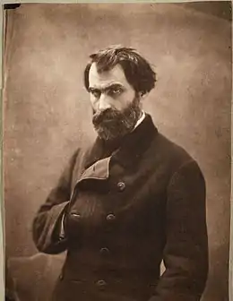Photographie sépia d’Eugène Pelletan, homme brun au regard perçant, tête nue, portant la barbe, la main droite glissée dans sa redingote à la manière de l’empereur Napoléon 1er.
