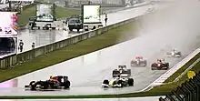 Photo de plusieurs monoplaces de Formule 1 roulant sous la pluie, à l'approche d'un virage