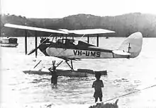 Single-engined biplane on floats, parked on the water with two boys in foreground