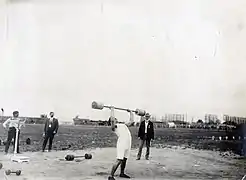 Photographie en noir et blanc d'un homme soulevant une barre avec deux poids au dessus de sa tête