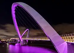 Un pont, tenu par une arche inclinée, éclairé de violet.