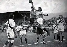 Photographie d'une scène d'un match de football : un gardien s'étend en l'air pour capter le ballon.