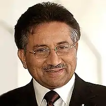Photo d'un homme souriant aux cheveux grisonnants et portant une moustache, en costume