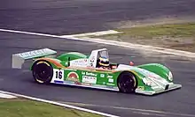 Photographie en couleur d'une voiture d'endurance blanche et verte, vue de trois-quarts droite, sur une piste sèche.