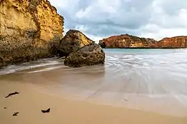Sur une plage de sable, s'écoulant le long d'un rocher, une vague en se retirant dessine une courbe harmonieuse.