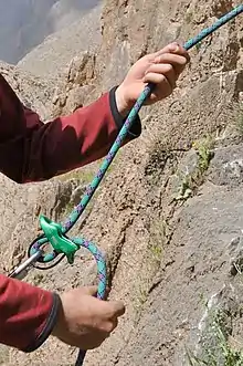 Un alpiniste tient dans ses mains une corde, qui traverse un appareil Reverso et un mousqueton.