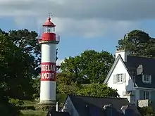 Phare rouge et blanc au soleil couchant avec pour inscription Doëlan Amont