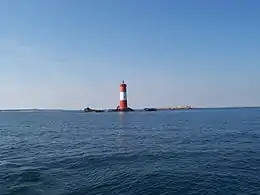 Vue d’un phare sur un îlot rocheux, au milieu de la mer.