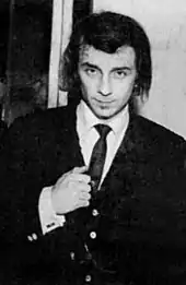 Photographie en noir et blanc d'un homme en costume et cravate noirs serrant le poing droit.