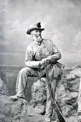 Photographie en noir et blanc d'un homme posant avec un fusil.