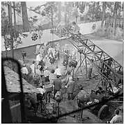 Photographie en noir et blanc prise en plongée lors du tournage du film, l’équipe technique est au premier plan et les acteurs au second plan.