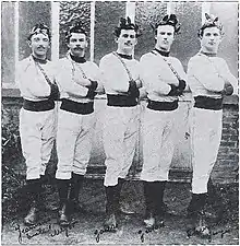 Cinq athlètes prenant la pose en tenue, bras croisés et avec une couronne de feuilles sur la tête