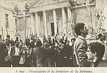 photographie en noir et blanc d'hommes brandissant de longs bouts de bois en face de la Sorbonne