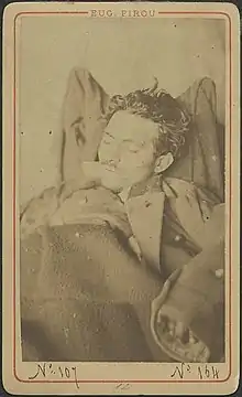 Photographie sépia du cadavre d'un homme jeune, portant une légère moustache, les yeux clos.
