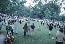 Photo en couleur d'une foule réunie dans un parc arboré