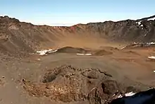 Cratère vu depuis sa paroi, avec des roches de couleur ocre.