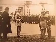 Homme en chapeau haut de forme et militaires lors d'une cérémonie de remise de décorations.