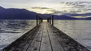 Un lac couronné de montagne ; au milieu surgit un quai de bois qui, par une illusion d'optique, traverse tout le lac et rejoint les montagnes.