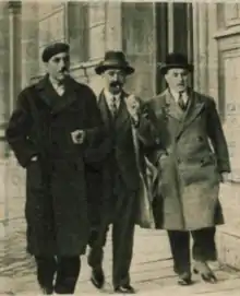 Bonny, sans cravate, en béret, la cigarette aux lèvres et l'allure négligée, escorté par deux policiers.