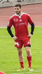 Un joueur de rugby de face, à l'arrêt et les mains sur les hanches.