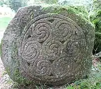 Face d'une pierre gravée de triskèles sur le chemin de ronde du camp celtique de la Bure.