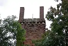Vue du sommet d'un édifice en briques, couronné à chacun de ses angles d'une colonne de section carrée en briques.