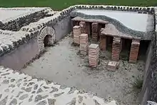 Photographie d'une série de briques empilées supportant le sol en béton d'une pièce antique.