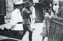 Photographie d'une scène représentant des soldats allemands saluant et regardant une femme portant un meuble.