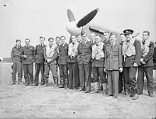 Photographie en noir et blanc d'un groupe d'hommes posant devant un avion.